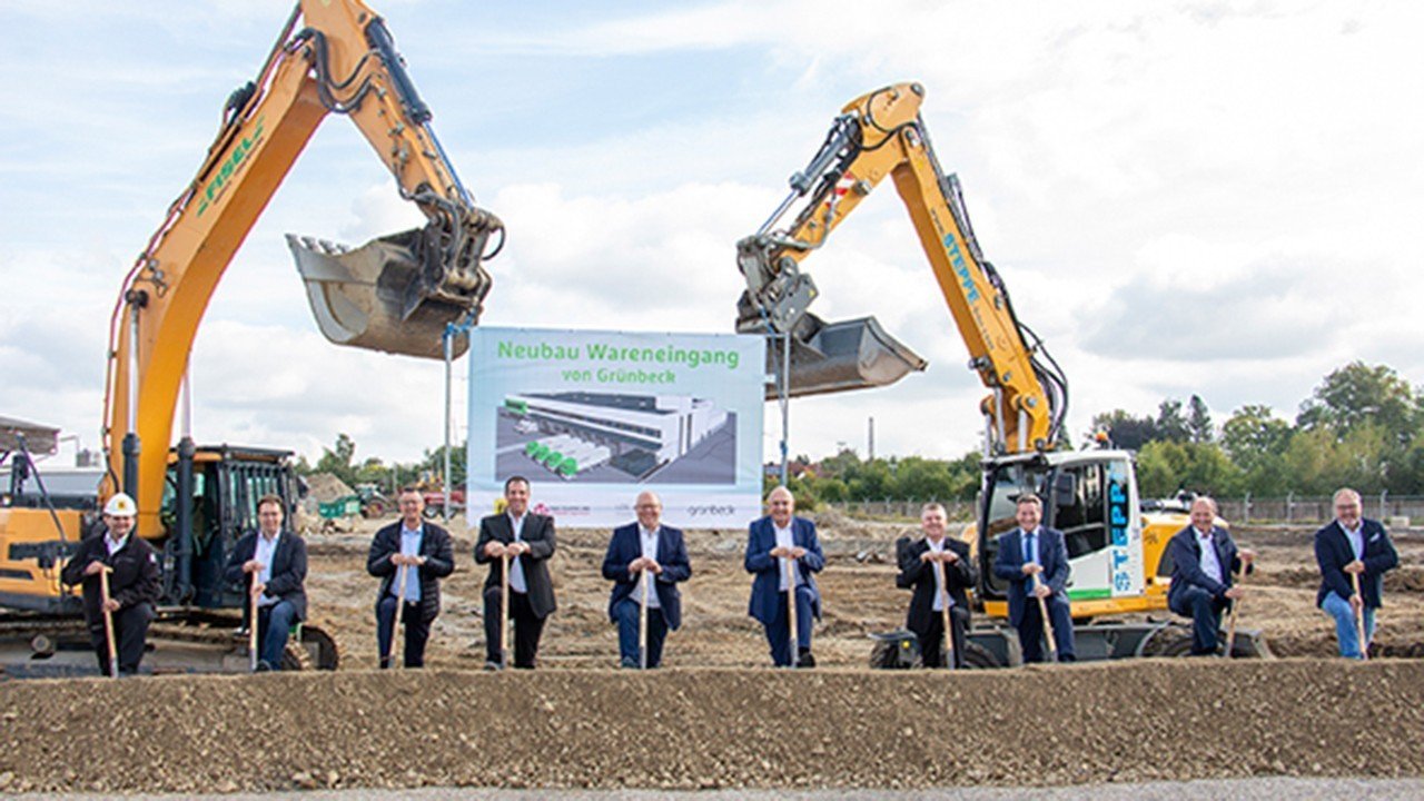 Eine Gruppe von Männern steht vor einem Bagger mit Schaufeln in den Händen